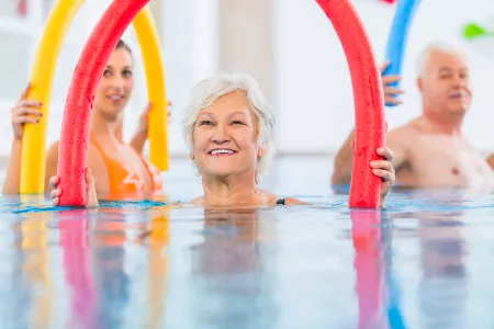 Eine Gruppe von Senioren beim Aquafitness-Training im Schwimmbad mit Poolnudeln