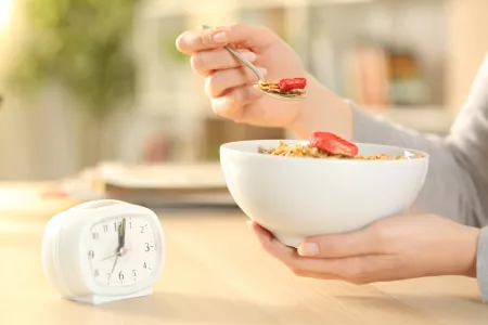 Nahaufnahme von Händen von Frauen, die eine Getreideschüssel mit Obst essen, nachdem sie intermittierende Basenfasten auf einem Tisch zu Hause sitzt