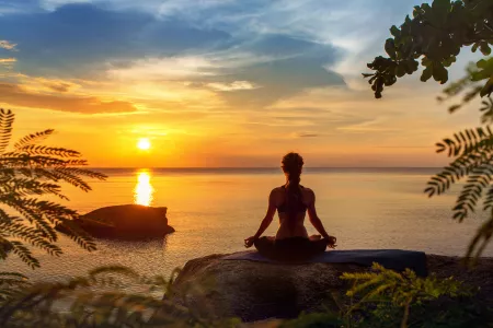 Frau praktiziert Yoga bei Sonnenuntergang am Strand während eines Meditation-Retreats