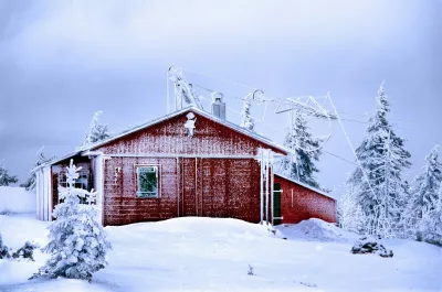 schneebedecktes rotes und graues Haus, umgeben von Bäumen, bei Tag