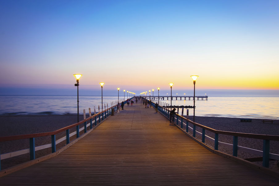 Beleuchteter romantischer Vintage-Pier in Palanga nach Sonnenuntergang mit Menschen, die an einem schönen Sommerabend spazieren gehen