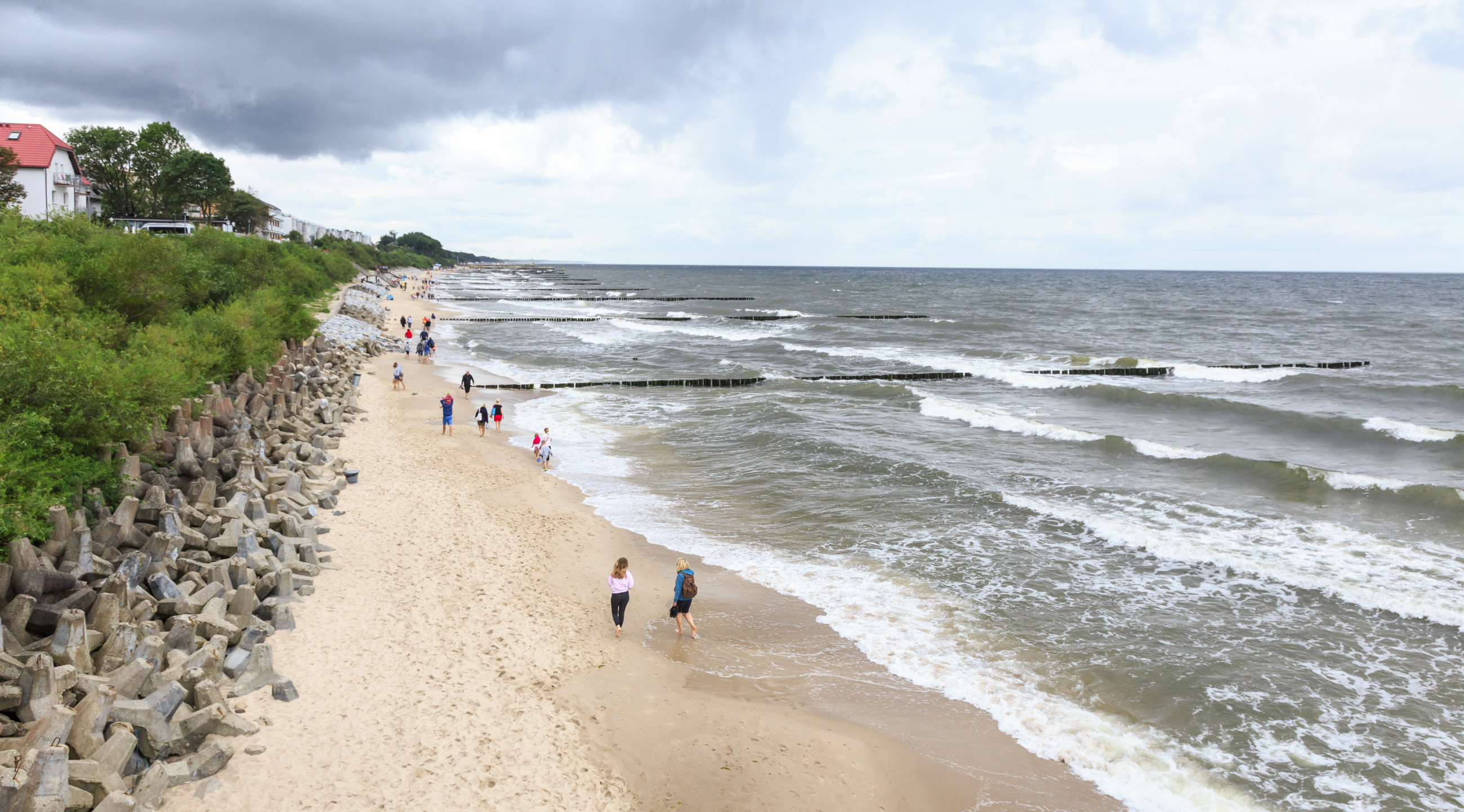 Spaziergänger am Strand in Ustronie Morskie bei bewölktem Wetter